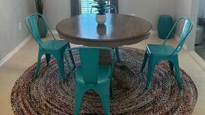 A dining area with a round table, four turquoise chairs, a chandelier, a mirror, and a decorative rug.