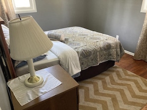 A bedroom with a bed, a nightstand with a lamp, a patterned rug, and a window with curtains.