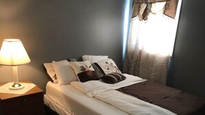 A bedroom with a bed, a nightstand, a lamp, and a window with curtains.