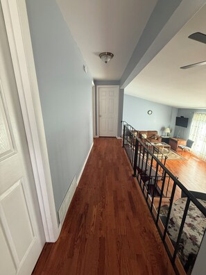 A hallway with wooden flooring, a white door, and a staircase leading to a living area with a sofa and a coffee table. - The Paradise @ Lyncott, A famiily friendly place to stay! (Lansing)