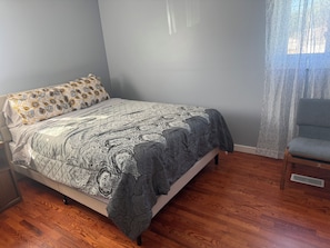 A bedroom with a bed, a chair, a window with curtains, and a wooden floor. - The Paradise @ Lyncott, A famiily friendly place to stay! (Lansing)