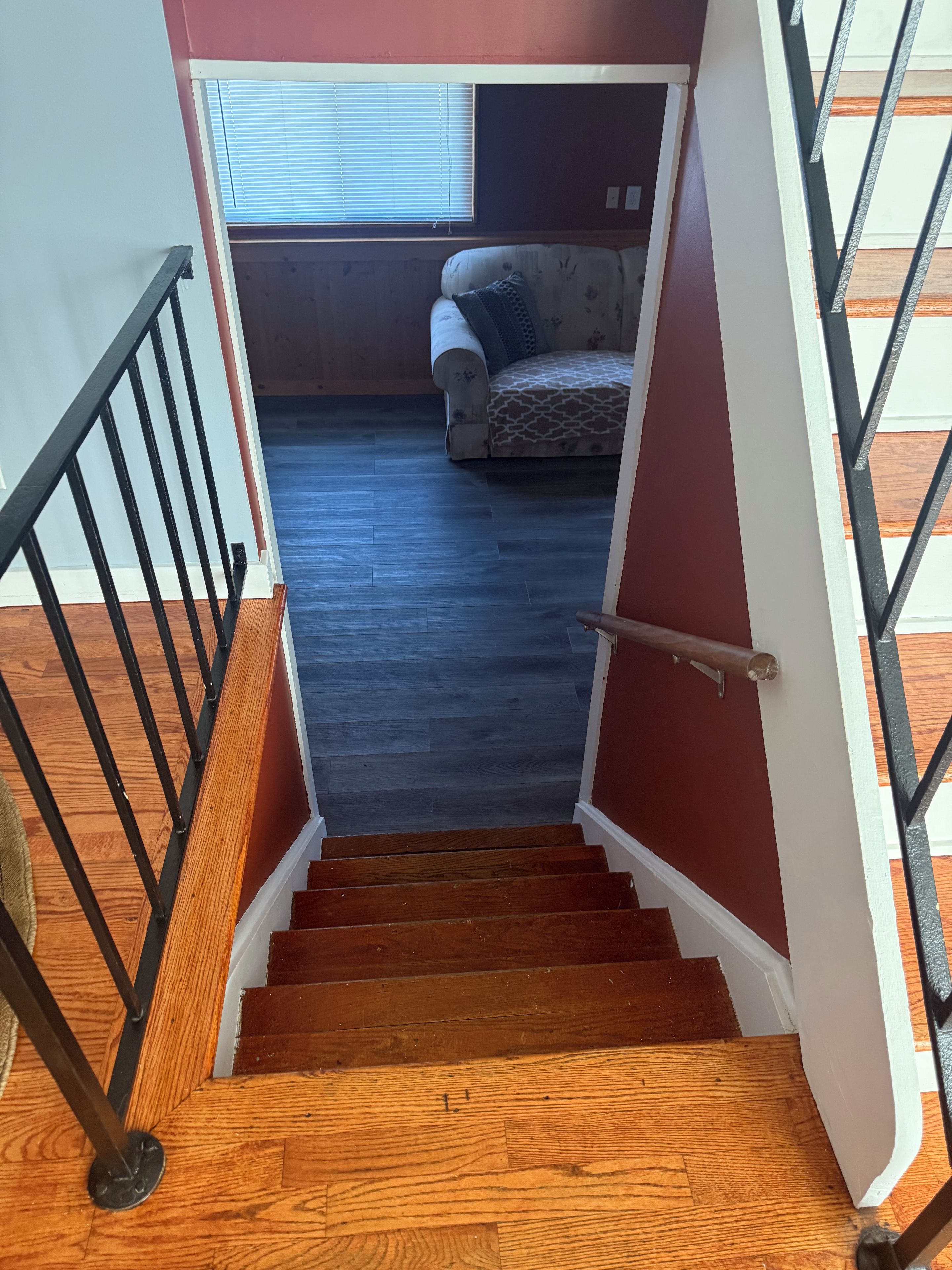 A staircase leading to a room with a patterned sofa and a window with blinds.