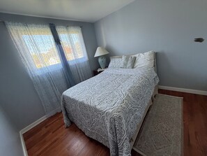 A bedroom with a bed, a nightstand, a lamp, a window with curtains, and a rug.