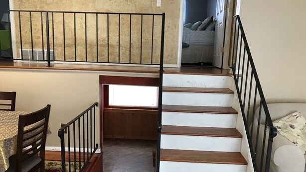 A staircase with wooden steps and black railings, leading to a landing with a view of a bedroom.