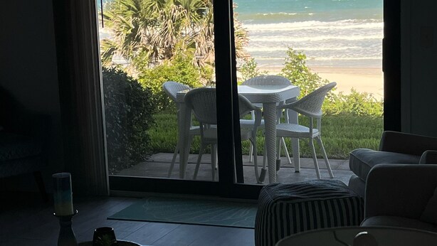 Een kamer met uitzicht op het strand, met een eethoek met tafel en stoelen, een bank en een lamp.