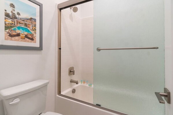 Une salle de bain avec une douche à parois de verre, des toilettes et un tableau représentant une piscine.