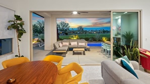 A modern living room with a sofa, coffee table, and chairs. There is a dining table with chairs. The room has large windows with a view of the outdoors. - Private pool & putting green - PGA WEST (La Quinta)