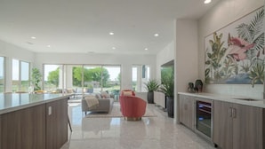 A spacious kitchen with a central island, a dining area with a sofa and chairs, and a large window providing natural light. - Private pool & putting green - PGA WEST (La Quinta)