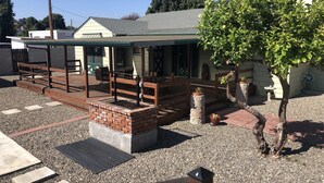 A covered outdoor seating area with a brick fireplace, surrounded by gravel and potted plants. - The “Clubhouse” in the Village of Arroyo Grande (Arroyo Grande)