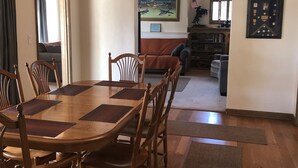 A dining area with a wooden table and chairs, a ceiling light, and a view of a living room with a couch and a bookshelf. - The “Clubhouse” in the Village of Arroyo Grande (Arroyo Grande)
