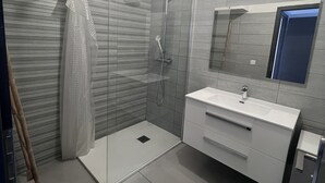 A modern bathroom with a glass shower enclosure, a white vanity with a mirror, and grey tiled walls. - Villa Avec Jacuzzi la Cadiere Dazur (La Cadière-d'Azur)