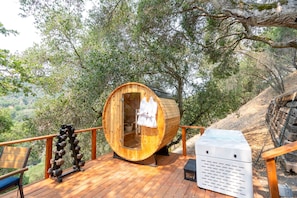 Estructura de sauna de madera con un banco y una mesa de masaje, rodeada por una terraza y árboles.