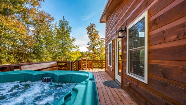 Una cabaña de madera con un jacuzzi en una terraza, rodeada de árboles.