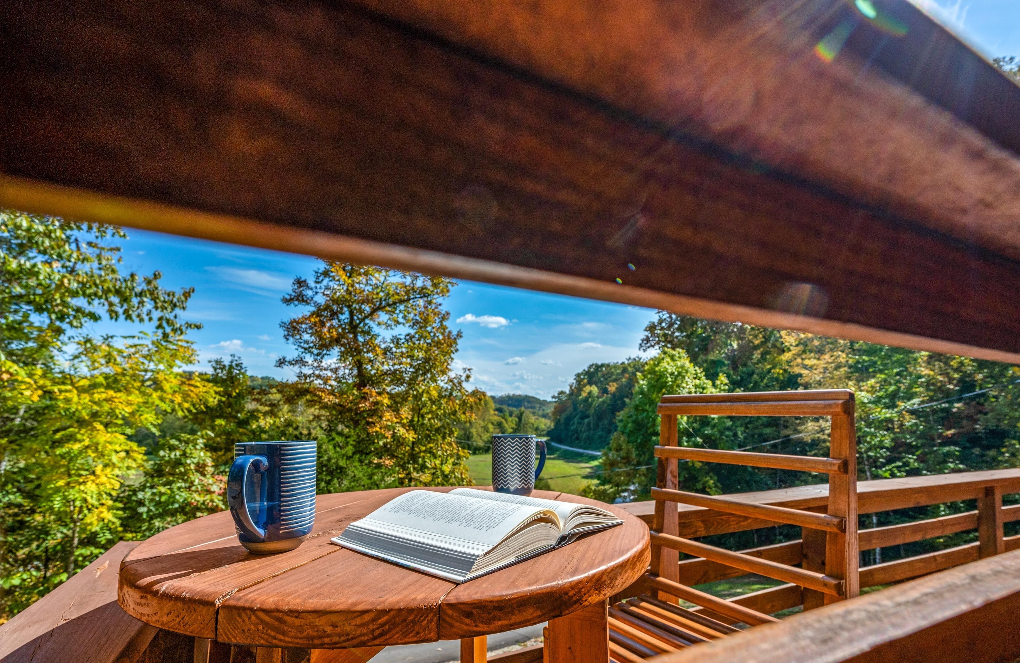 Una mesa de madera con un libro y una taza, con vistas a un paisaje pintoresco.