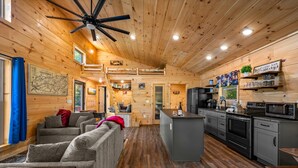 Un interior de cabaña acogedor, con techo de madera, una kitchenette, una zona de estar con sofá y mesa, y una pequeña barra.