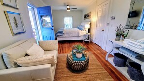 Una habitación compacta con cama, mesita de noche, sofá, una mesa baja con una planta y un estante con toallas dobladas.