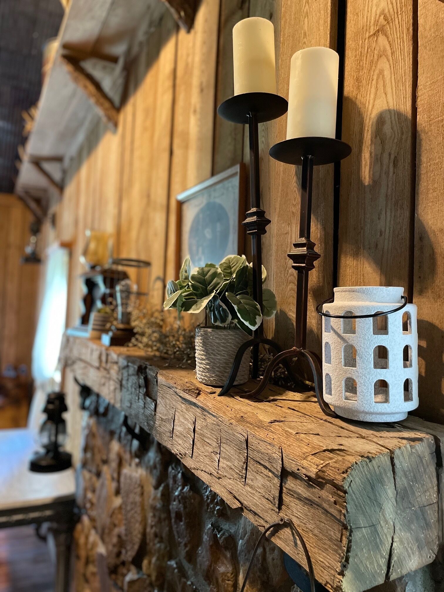 Una estantería de madera rústica con velas, una planta en maceta y un farol blanco texturizado.