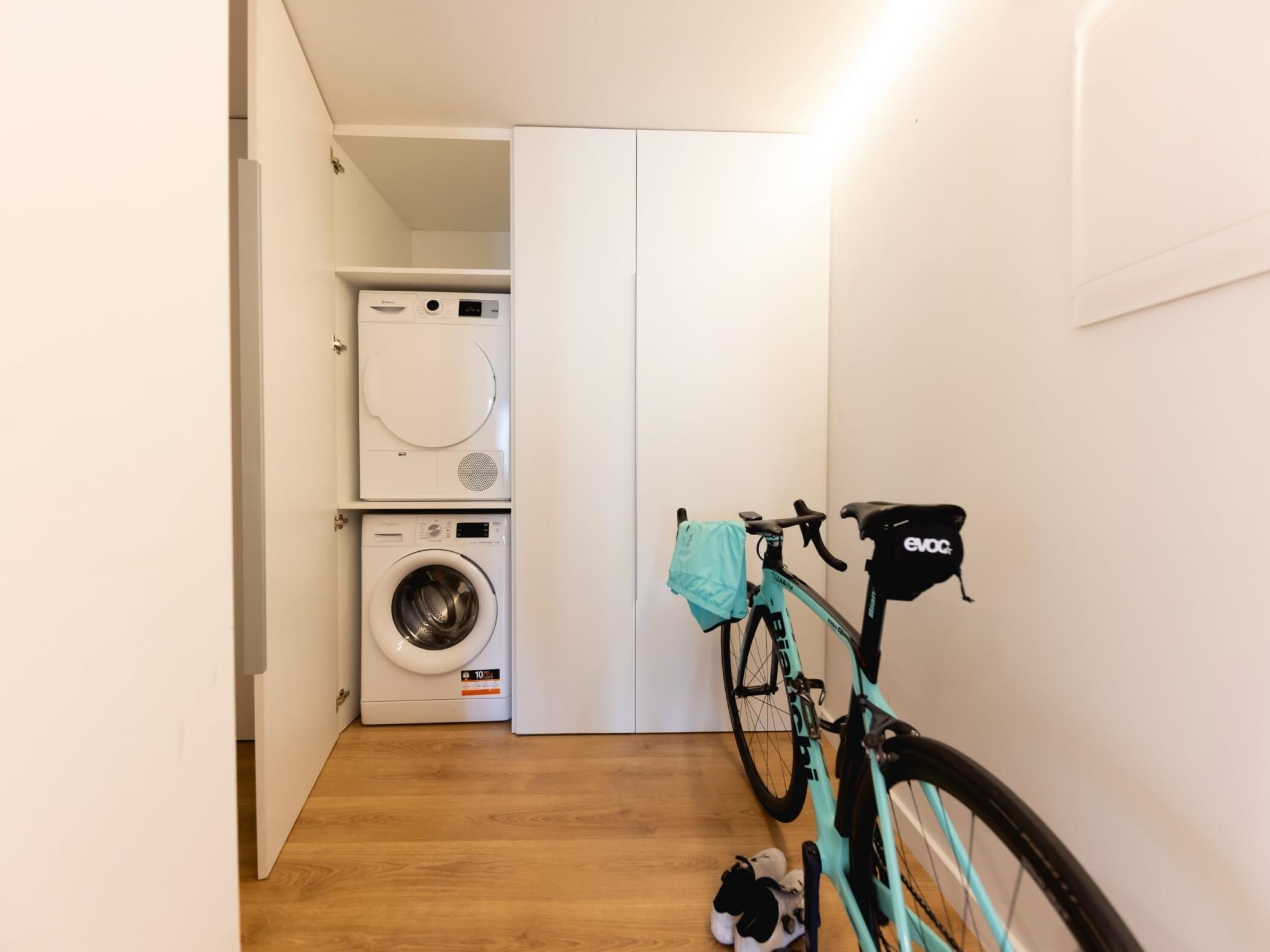 Ein Waschbereich mit Waschmaschine und Trockner, ein Fahrrad mit türkisem Rahmen und ein Paar Schuhe auf dem Boden.