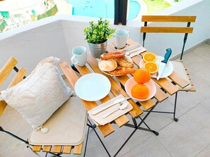 A wooden table with breakfast items, a white cushion, and a view of a swimming pool.