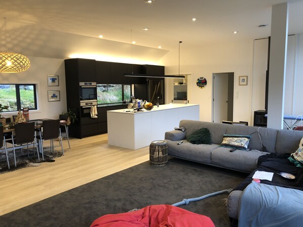 Contemporary living space with a central kitchen area, dining table, and large window offering a view of the outdoors.