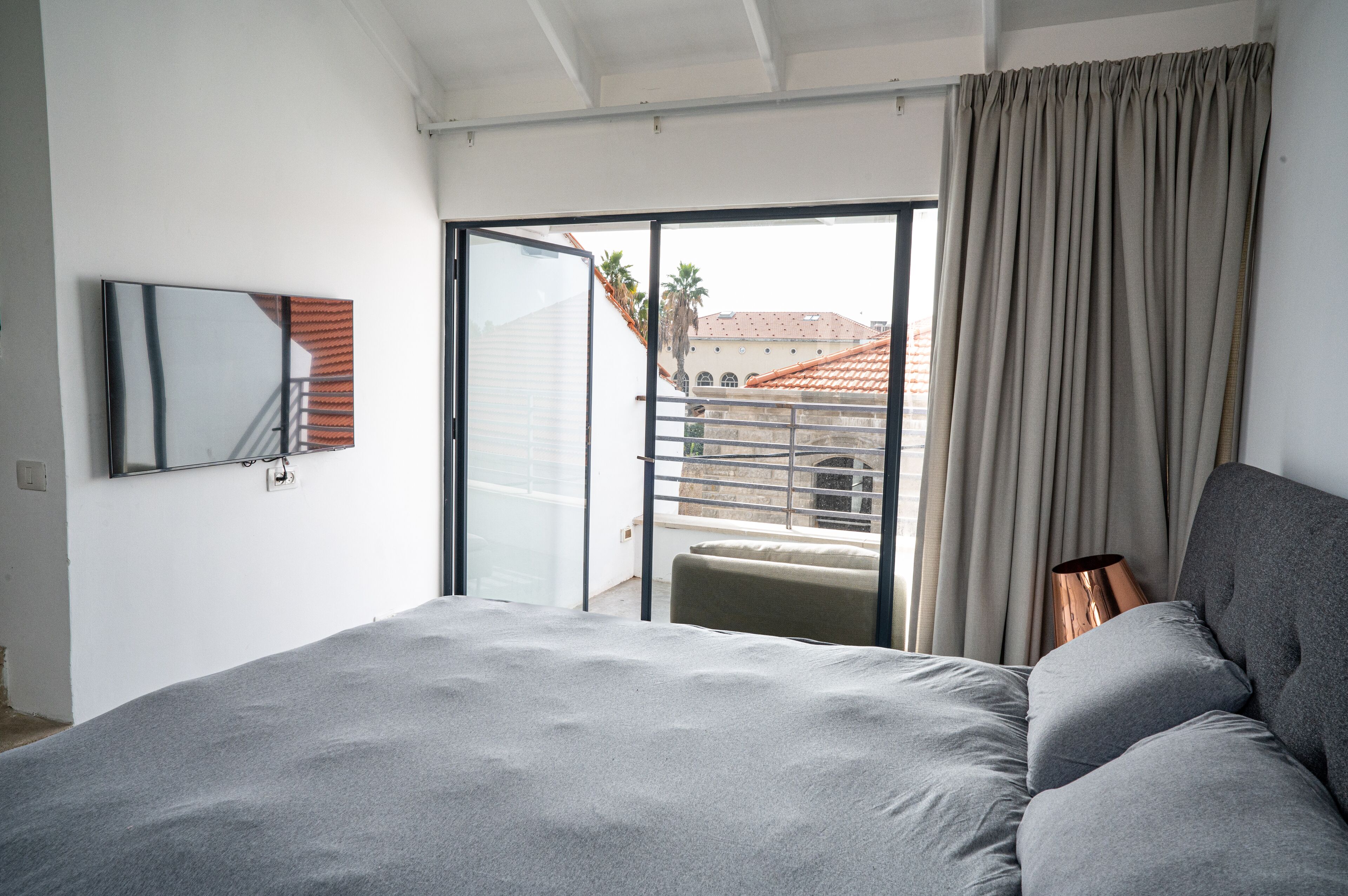 Une chambre avec un lit, une porte-fenêtre coulissante donnant sur un balcon, un téléviseur à écran plat et une vue sur les immeubles.