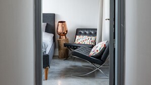 Un couloir étroit mène à une chambre où se trouvent un lit, une chaise, une lampe et un petit tabouret en bois.