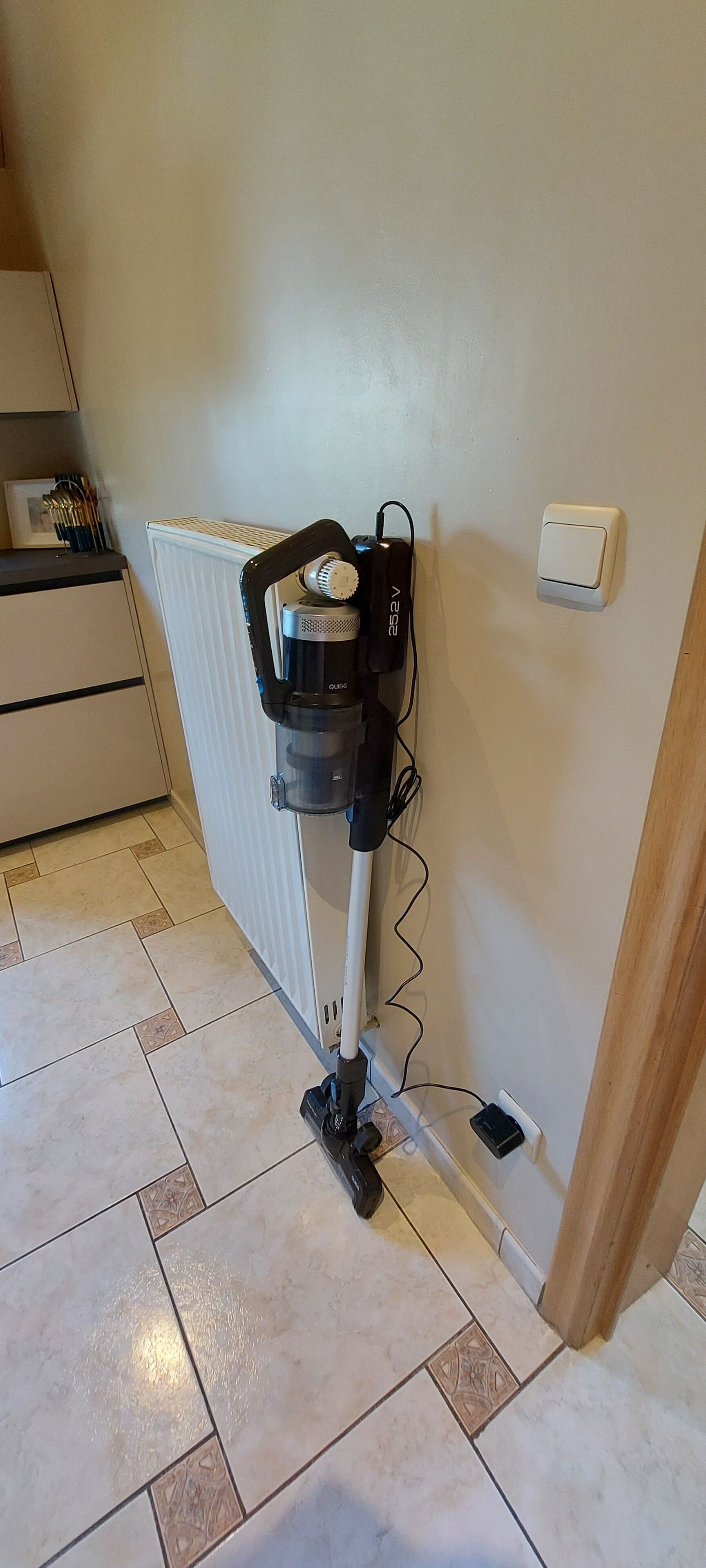 Un aspirateur appuyé contre un mur, près d’un radiateur, d’une prise de courant et d’un interrupteur.
