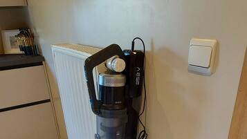 Un aspirateur appuyé contre un mur, près d’un radiateur, d’une prise de courant et d’un interrupteur.