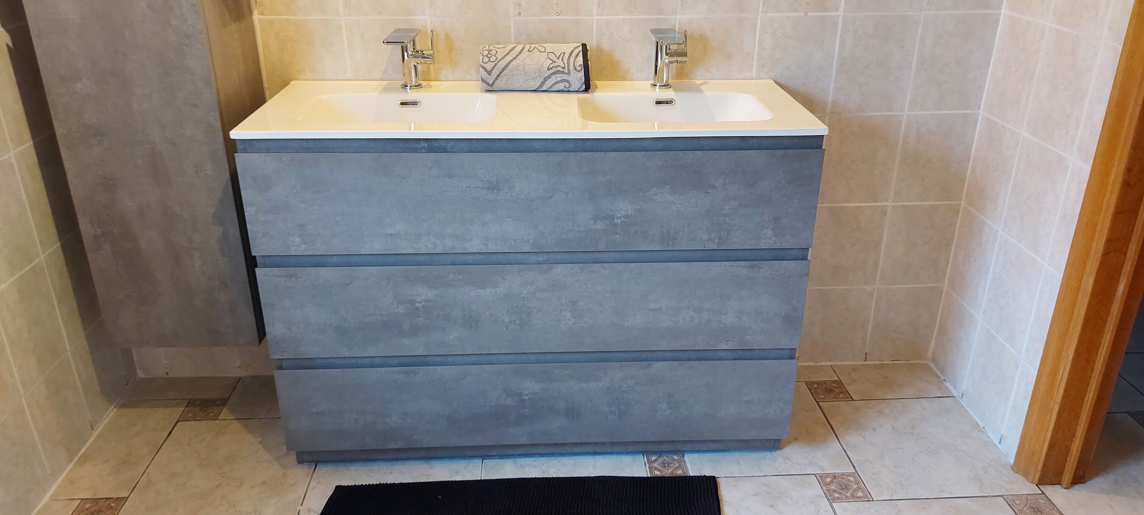 Un baño con dos lavamanos, pared de azulejos de mármol y un mueble de color gris.