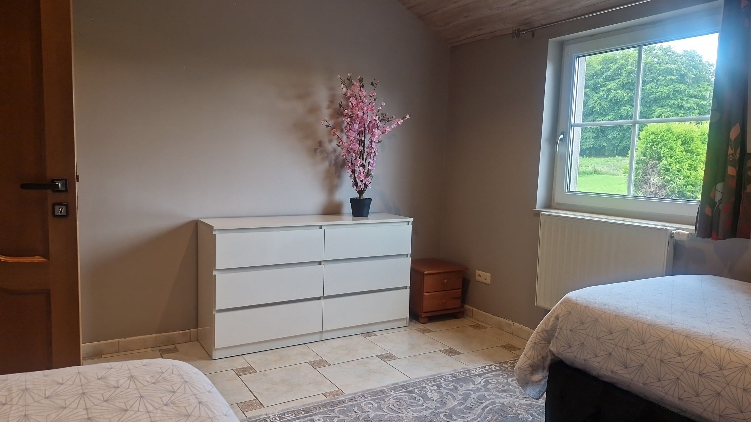 Quarto com penteadeira branca, janela com vista para vegetação e colcha estampada.