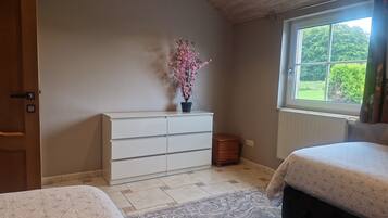 Quarto com penteadeira branca, janela com vista para vegetação e colcha estampada.