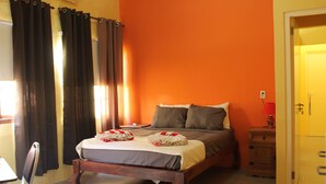 A neatly made bed with pillows and a blanket, a wooden nightstand with a lamp, and a chair in a room with orange walls. - Nice & private in our backyard with own entry & parking lot. (Willemstad)