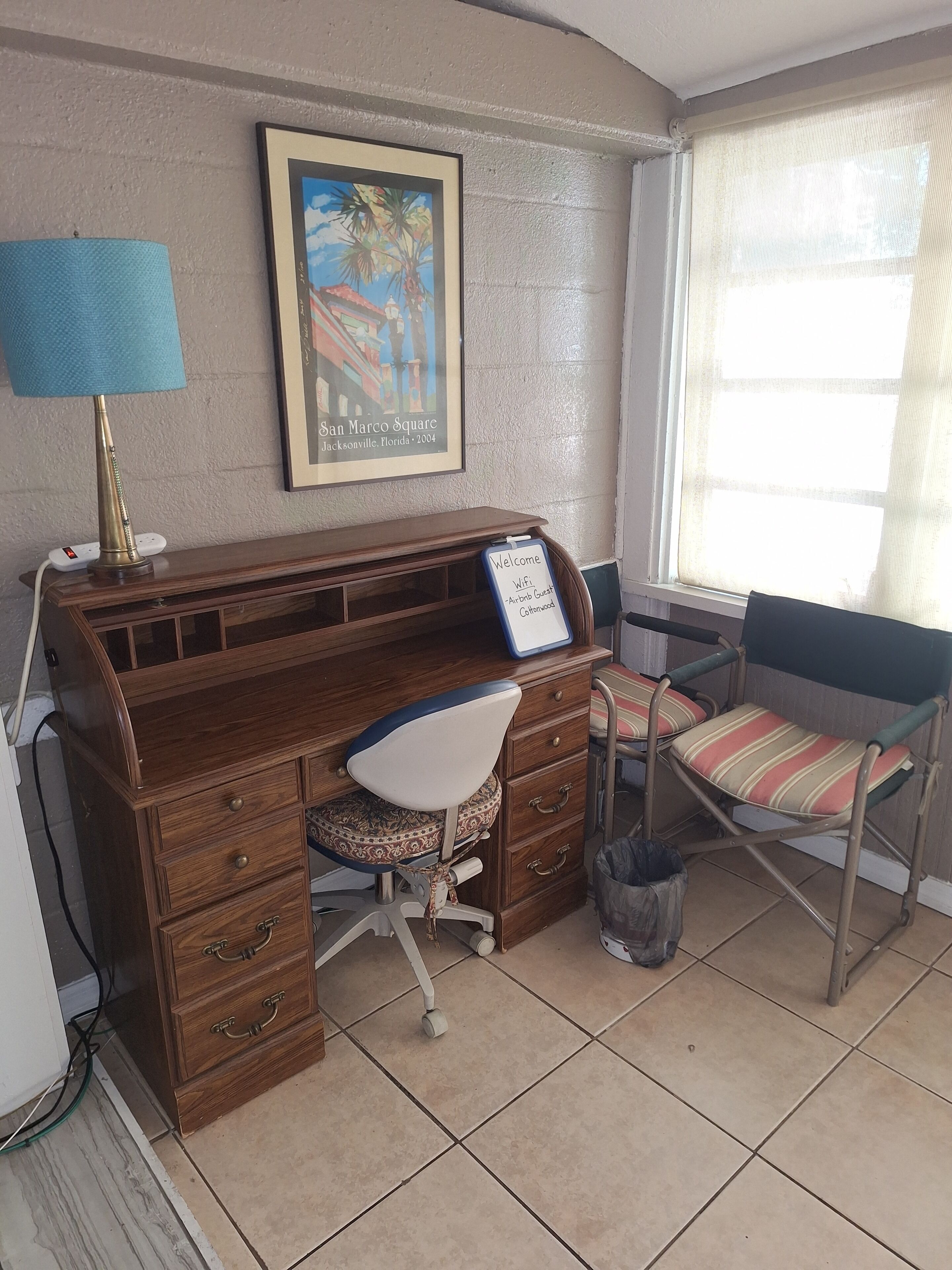 Un escritorio de madera con una silla, un cuadro en la pared y una ventana con vistas.