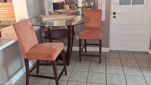 A dining area with a glass table, two chairs, a white door, and a tiled floor.