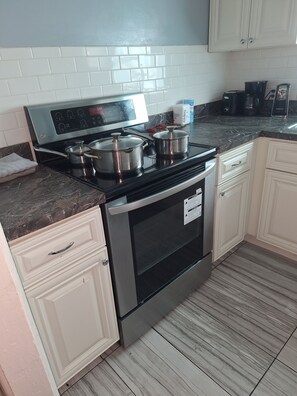 Una cocina con estufa de acero inoxidable, armarios blancos y salpicadero de azulejos.