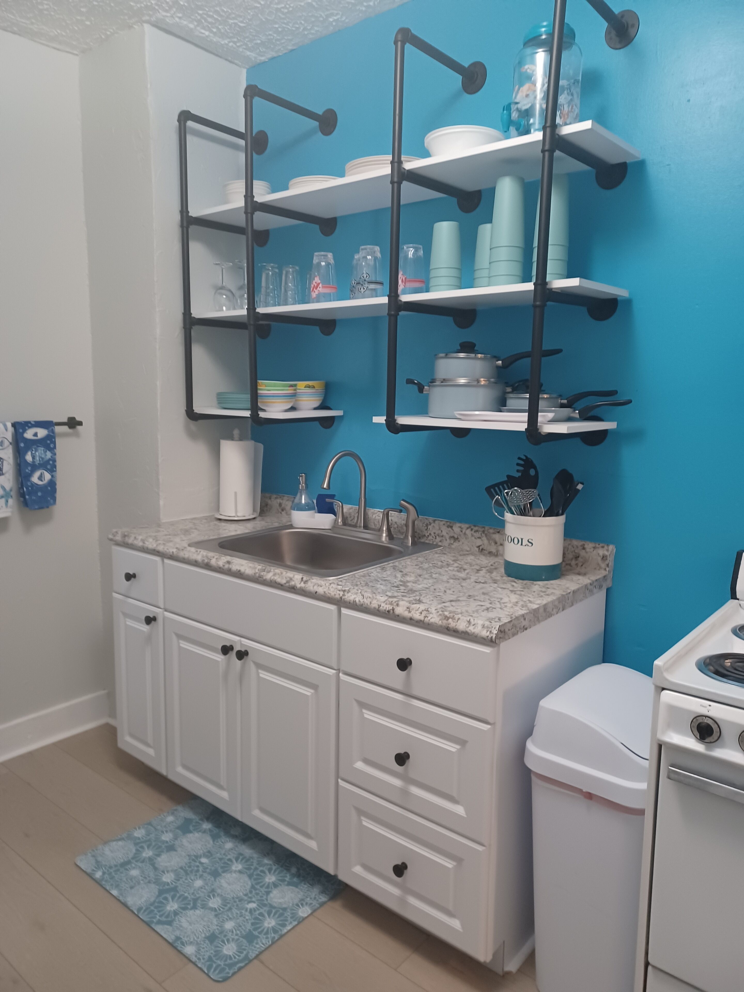 A kitchen with white cabinets, a granite countertop, a sink, a stove, and shelves with dishes and utensils.