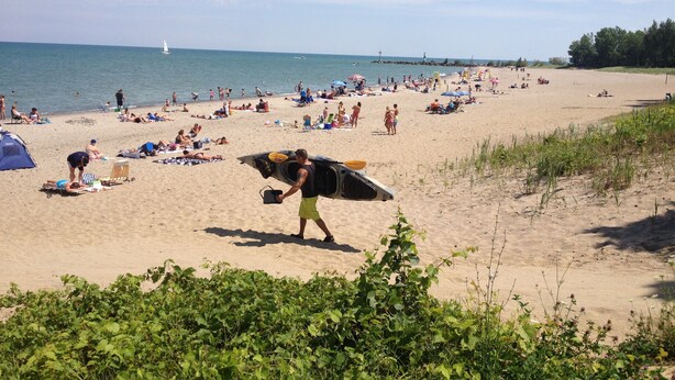 Ein Strand mit badenden und spazierenden Personen, einem Zelt und einem Rettungsturm.