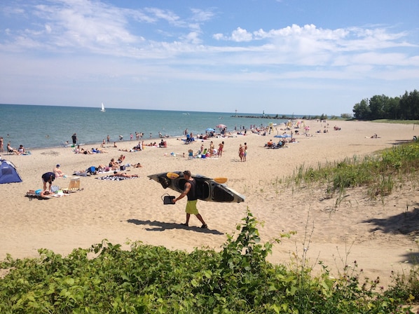 Une plage où l’on voit des gens se prélasser au soleil et se promener, une tente et un poste de surveillance des sauveteurs.