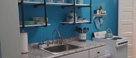 A kitchen with white cabinets, a sink, a stove, and shelves with kitchenware.