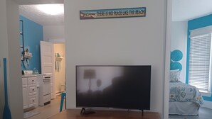 Ein Wohnzimmer mit Fernseher auf Holzständer, einer blauen Yogamatte und einem Wandschild.