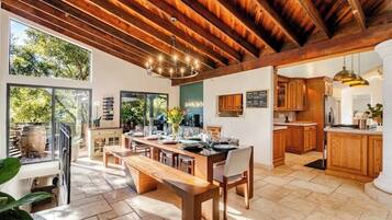 A spacious kitchen with wooden cabinets, a dining area with a bench, and large windows offering views of greenery.