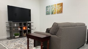 Ein modernes Wohnzimmer mit einem grauen Sofa, einem Holztisch, einem Flachbildfernseher auf einem Holzständer, einem gemusterten Teppich und drei Wandbildern.