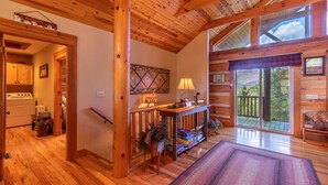 Interior de una cabaña de madera con cocina, comedor con mesa y sillas, y un amplio ventanal corredera que da a una terraza.