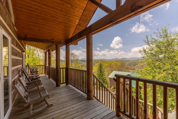 A wooden deck with rocking chairs and a view of a mountain landscape.