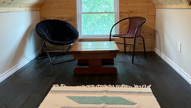 A cozy attic room with a sloped wooden ceiling, a window with a view of greenery, and a small wooden table with two chairs. - Spacious house, 5 min walk to downtown- cafes, restaurants, and pubs (Peterborough)