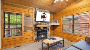 A cozy cabin interior with a stone fireplace, wooden walls, and a ceiling fan. - Cozy Cabin for Two near Shows! Whirlpool Tub, Gas Fireplace, Private Balcony (Branson)
