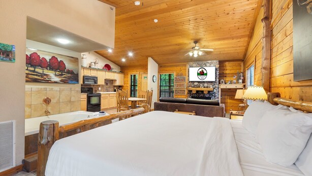 A wooden cabin-style room with a large bed, a dining table, and a kitchen area. - Cozy Cabin for Two near Shows! Whirlpool Tub, Gas Fireplace, Private Balcony (Branson)