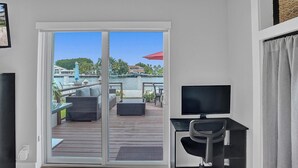 Een kamer met een schuifdeur die uitkomt op een terras met tuinmeubilair, een televisie en een bureau.