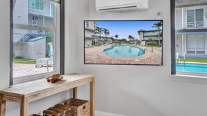 Een kamer met een grote televisie waarop een zwembad zichtbaar is, een houten tafel en een airconditioning.