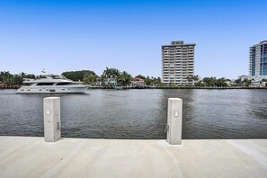 A waterfront view with a yacht docked at a pier, a tall building, and a palm tree-lined promenade.